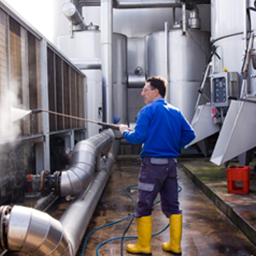 Man providing industrial cleaning in Peoria IL by pressure washing large machinery