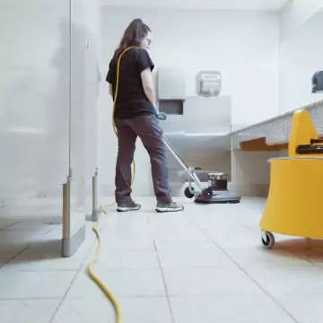 A cleaner is seen cleaning a public restroom. Corporate Clean can tell you "What is the role of a commercial cleaner?"