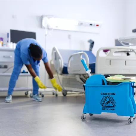 A member of the Corporate Clean team sweeps under a bed in a hospital room as part of her Healthcare cleaning services