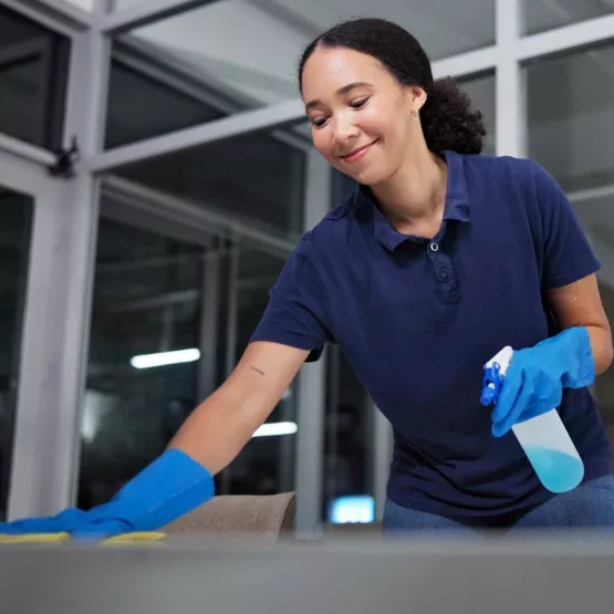 A woman wearing gloves and holding a spray bottle wipes down a corporate office as part of the Commercial Cleaning Services Corporate Clean offers
