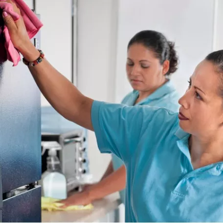 Two women wipe down surfaces in a company break room, which is one of the industries served by Corporate Clean