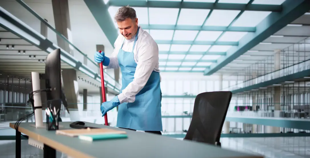 A man cleans around a desk at a corporate office, which is one of the industries served by Corporate Clean