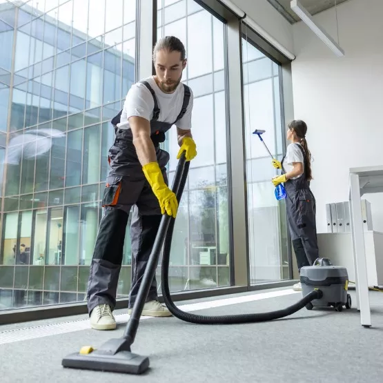 A man vacuums while a woman washes windows at a corporate office, which is one of the industries served by Corporate Clean