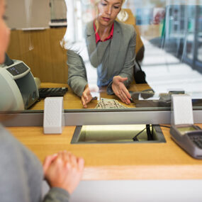 A woman receives cash from a bank teller in an area that’s been cleaned with banking cleaning services from Corporate Clean